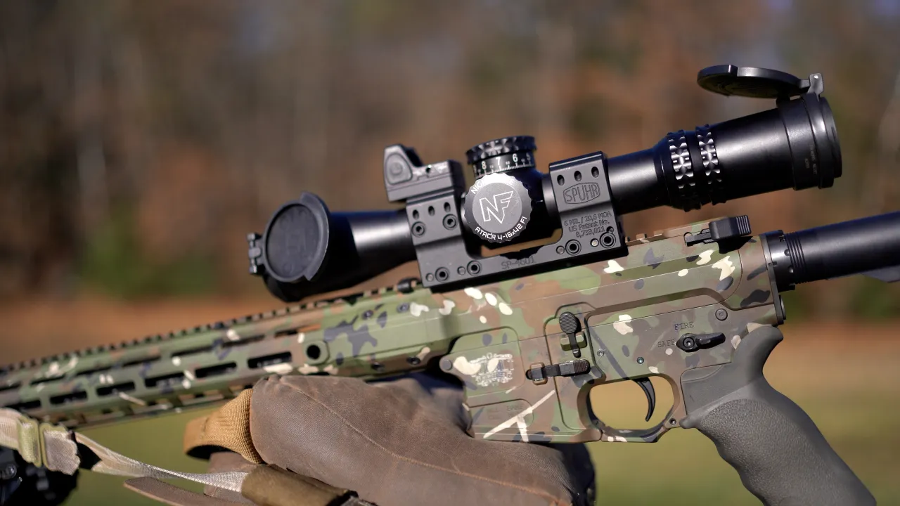 Close-up of a camouflage-finished precision AR rifle with a Nightforce scope, rested on a shooting bag