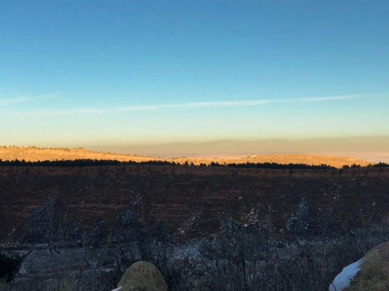 Sunrise over a wide valley seen from a snowy, rocky ridge