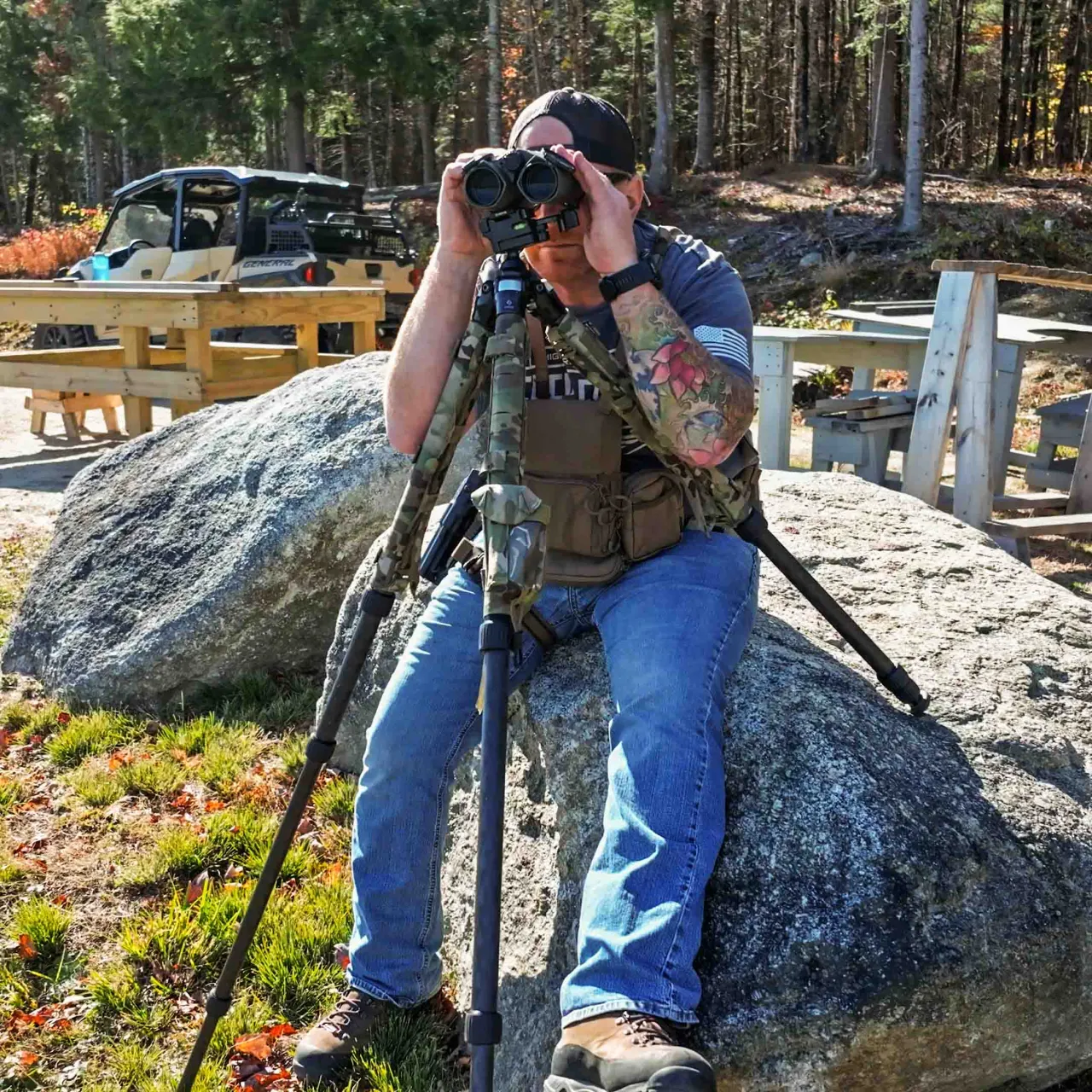 Student seated on a boulder looking through binoculars mounted on a tripod
