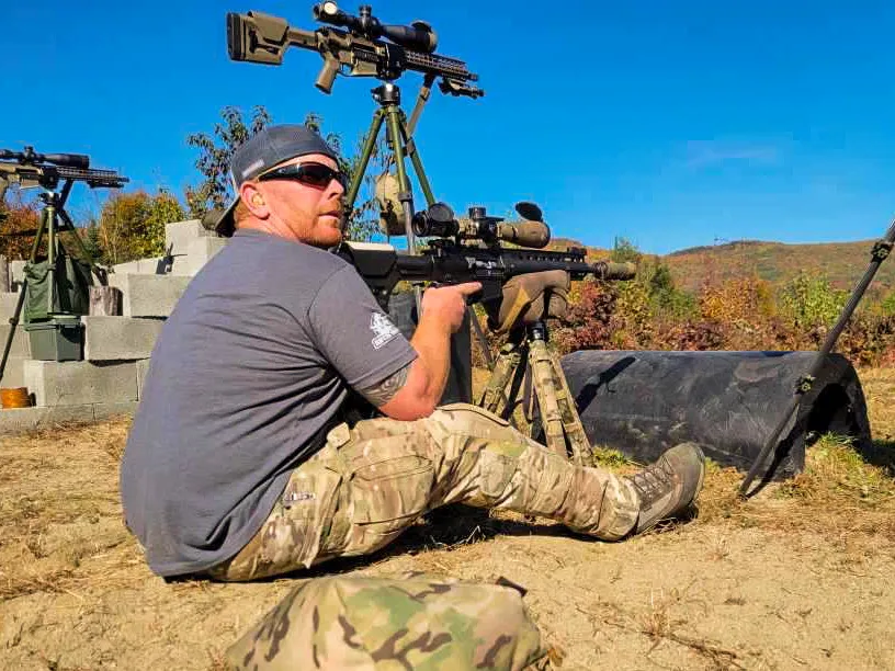 Student seated behind a rifle on a tripod at the range, with more rifles on tripods behind