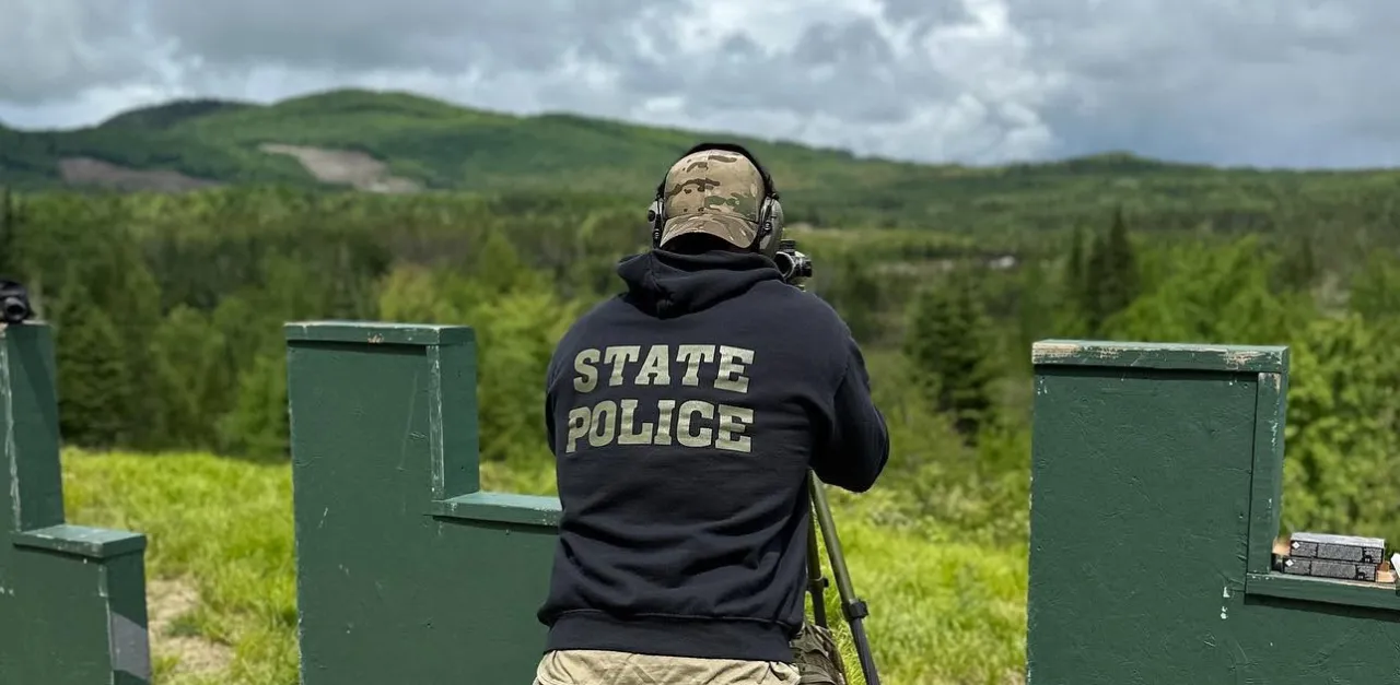 Officer in a State Police hoodie aiming from a tripod between green barricades at the range