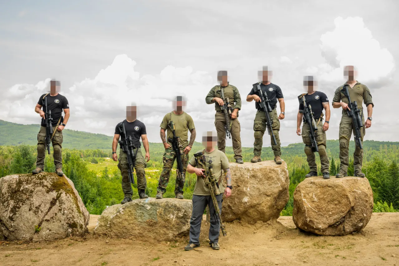 Class group with rifles standing on boulders in front of a green valley