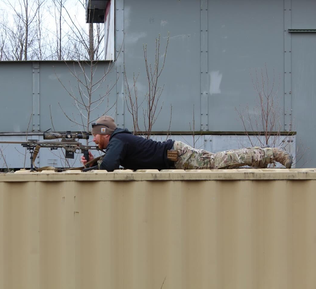 Shooter prone on top of a shipping container aiming a precision rifle